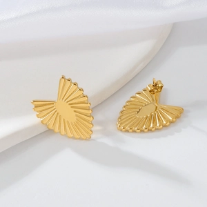 Close-up of golden heart earrings with radial textured lines on white stone and silk