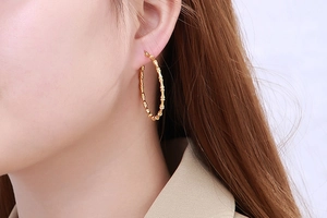Detailed view of large gold bamboo textured hoop earrings on a female model
