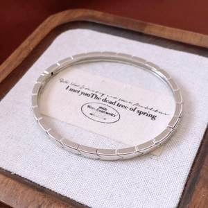 Gros plan d'un bracelet argenté géométrique avec textures facettées sur socle en bois