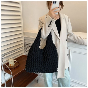 Detail of black pleated shoulder bag carried by model in a stylish beige blazer outfit