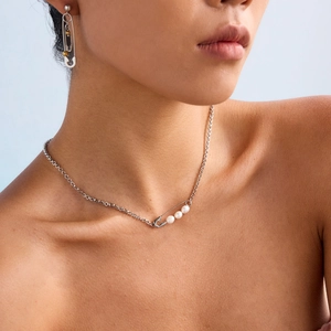 Close-up of a silver safety pin necklace and earrings set with white pearls on a model