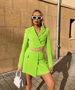Outdoor shot of a neon green cropped blazer and skirt set against a stone wall