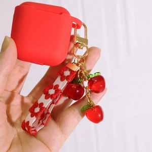 Red silicone AirPods case featuring translucent cherry charms and floral woven wrist strap