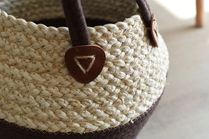 Detail of woven fiber and brown felt storage basket with leather handle and stitching