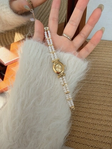 Close-up of vintage oval gold watch with double pearl bracelet on woman's wrist