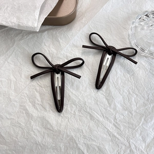 Détail de deux pinces à cheveux papillon en cuir marron foncé sur fond blanc épuré
