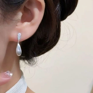 Detail of silver waterdrop earrings with zircon inlays worn by model on ear