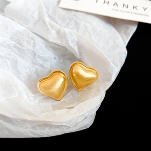 Close-up of heart-shaped gold stud earrings with a brushed metal matte texture on white paper