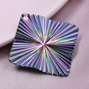 Macro shot of 18k plated rainbow rhombic pendant with radial texture on pink silk fabric