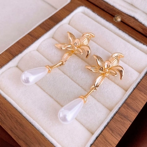 Close-up of gold-plated flower earrings with teardrop pearls on cream velvet lining