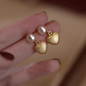 Brushed gold heart earrings with white freshwater pearls held by hand close-up
