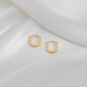 Detailed close-up of gold rectangular hoop earrings with bamboo texture on white silk fabric
