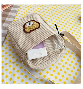 Close-up of beige corduroy crossbody bag with bear embroidery showing internal capacity