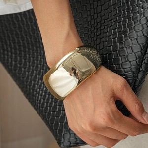 Macro view of wide gold mirror-polished metal cuff bracelet on wrist against leather background