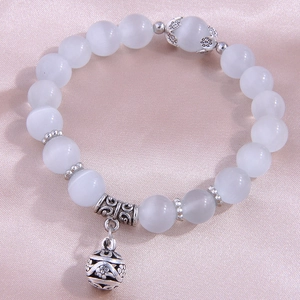 Cat's eye bead bracelet with silver hollow pendant on smooth silk background