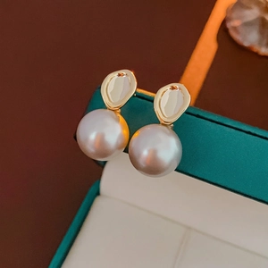 Clous dorés géométriques élégants avec perles blanches sur un écrin vert foncé
