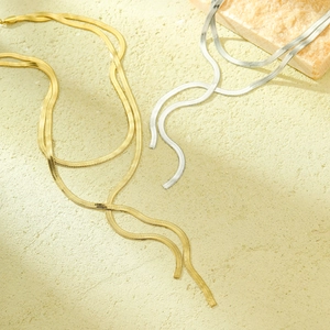 Gold and silver stainless steel flat snake chain necklaces on a textured warm background