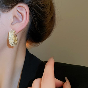 Detailed view of golden C-shaped hoop earrings with unique pleated texture on model