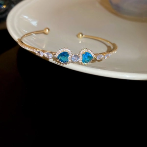Close-up of luxury gold open bangle with blue heart-shaped gems and sparkling zircons
