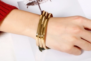 Macro detail of stacked gold square bangles with geometric facets on a model wrist