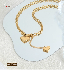 Detail of 18K gold plated titanium chain with dangling double heart pendants on mirror