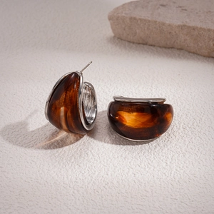 Detailed view of C-shape resin earrings with amber finish on a textured stone surface