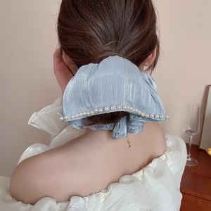 Close-up of a light blue satin floral scrunchie with pearls worn on a ponytail