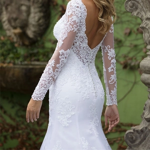 Elegant white lace wedding dress with deep V-neck and long sheer sleeves in garden setting