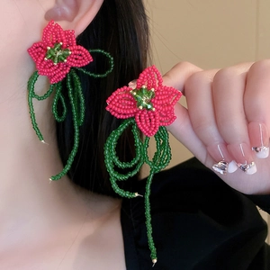 Detail of handmade woven red bead flower earrings with green beaded fringe on model