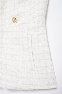 Close-up of white tweed fabric texture with gold button and side pocket detail