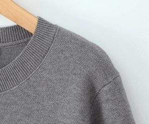 Close-up of grey knitted crewneck top showing ribbed collar and fine shoulder stitching