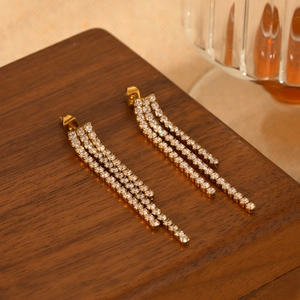 Elegant gold stainless steel tassel earrings with sparkling crystals on wood surface