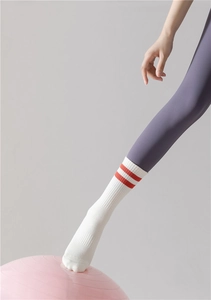 Chaussettes de yoga en coton blanc avec rayures rouges portées sur un ballon rose