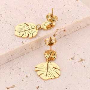 Macro detail of golden monstera leaf earrings on a natural pink stone surface
