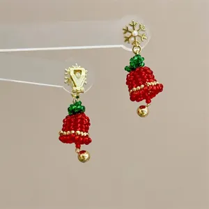 Macro detail of handmade beaded Christmas bell earrings with gold snowflake and red bow