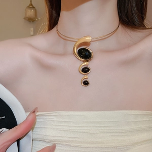 Detailed close-up of a gold wavy necklace with black resin oval stones on a model
