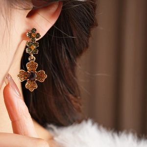 Gros plan d'une boucle d'oreille croix vintage ornée de pierres orange et violettes