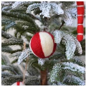 Detailed view of red and white striped wool felt ball ornament hanging on a snowy Christmas tree