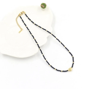 Chic beaded necklace with black faceted beads and a golden heart pendant on a white tray