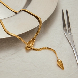 Nahaufnahme einer goldenen Schlangenkette mit Tropfenanhänger auf einer Leinenunterlage
