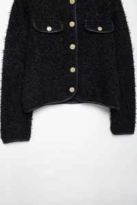 Détail de veste en tweed noir avec boutons dorés et bordures en cuir synthétique