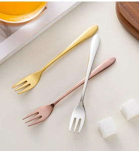 Flat lay of small metal dessert forks in gold, silver, and rose gold on a beige surface