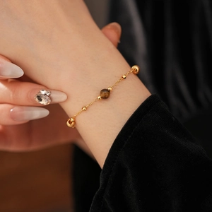Detail of a gold-plated pearl bracelet with a polished brown tiger eye stone on a wrist