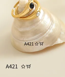 Detail of golden irregular rings featuring black stone and pearl on a shell base