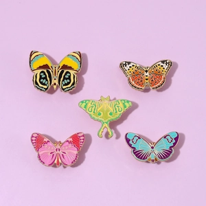 Set of five colorful butterfly and moth enamel pins with gold trim on purple background