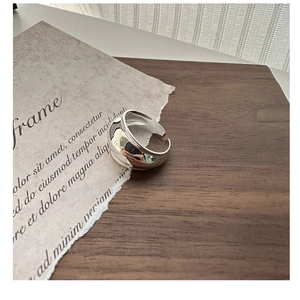 Close-up of a wide chunky silver ring on vintage paper, highlighting its sleek polished finish