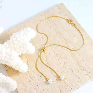 Adjustable gold snake chain bracelet with pearl tassels on a marble display tray