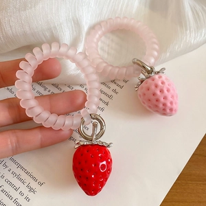 Détail de breloques fraises en peluche sur un élastique à cheveux spirale rose
