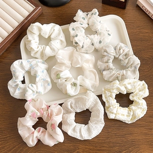 Flat lay of floral and solid scrunchies in pastel colors on a wooden tray with a book