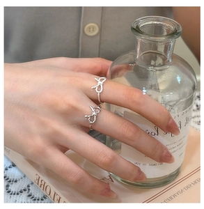 Detail of bow-shaped silver rings with textured knots and minimalist design on female hands